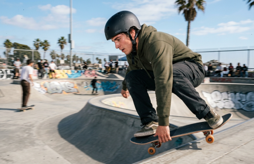 Skater wearing a certified matte black helmet at a sunny outdoor concrete skatepark.