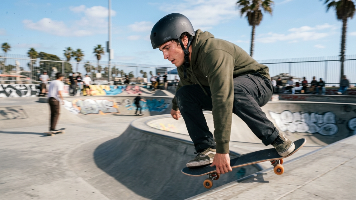 Skater wearing a certified matte black helmet at a sunny outdoor concrete skatepark.